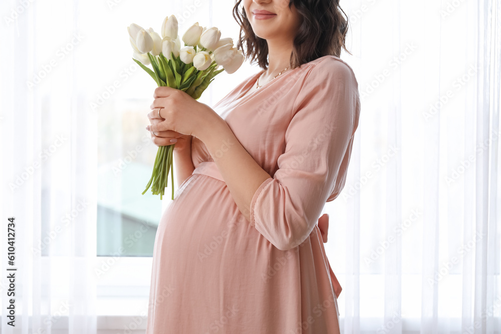 Young pregnant woman with tulips near window at home, closeup