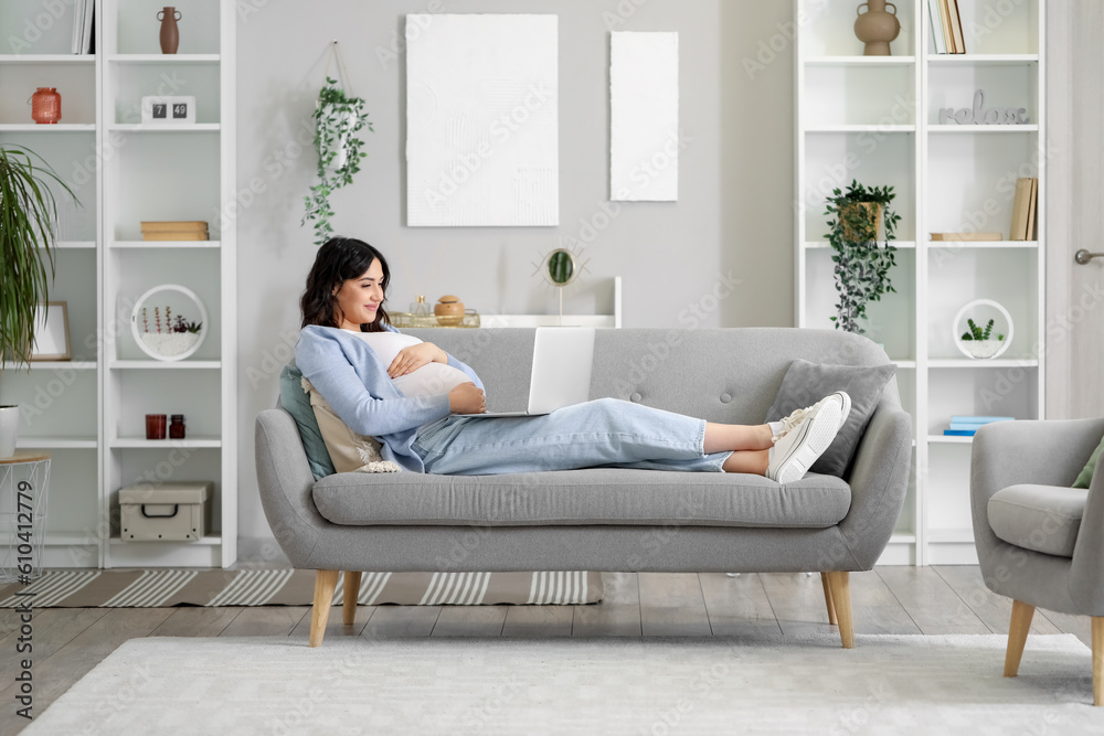 Young pregnant woman working with laptop on sofa at home