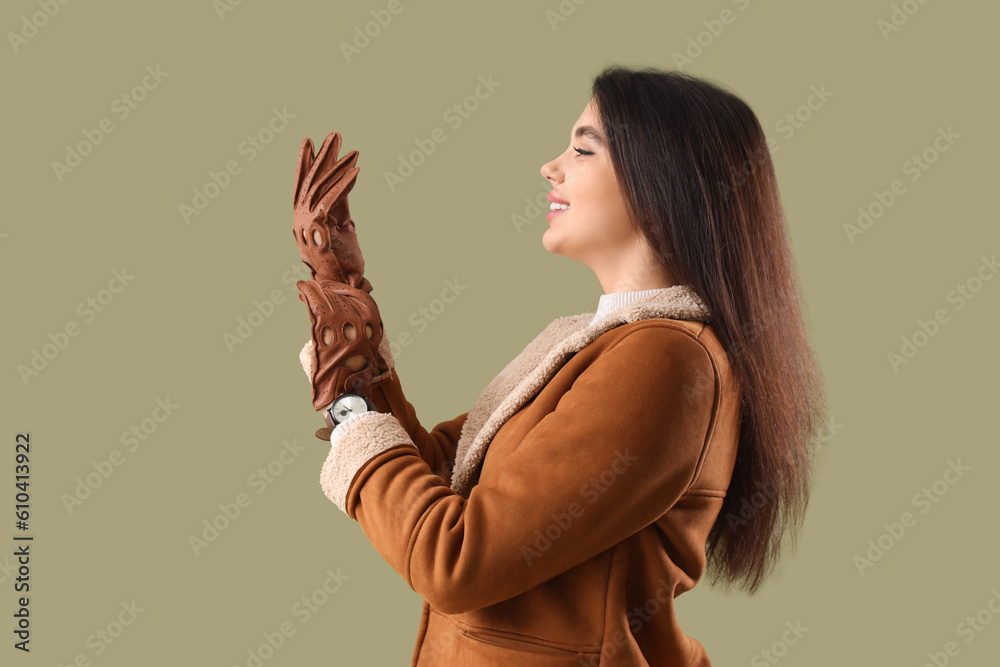 Stylish young woman in leather gloves on green background