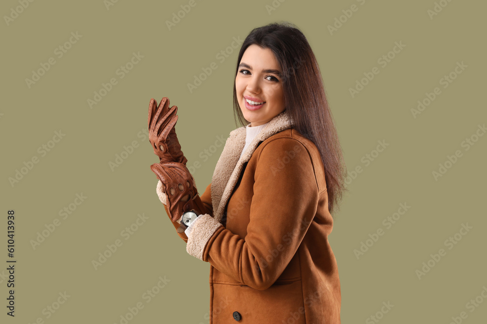 Stylish young woman in leather gloves on green background