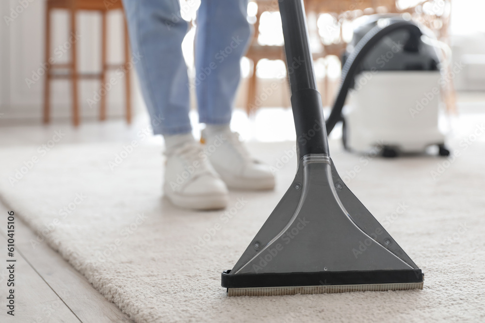 Young woman vacuuming carpet in kitchen