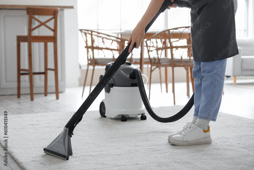 Young woman vacuuming carpet in kitchen