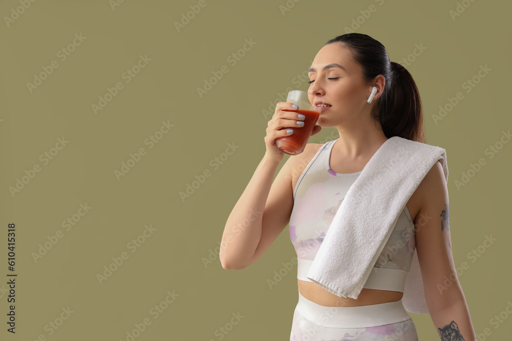 Sporty young woman drinking vegetable juice on green background