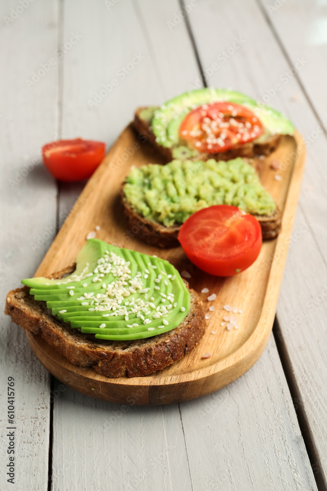 Board of tasty avocado toast on light wooden background