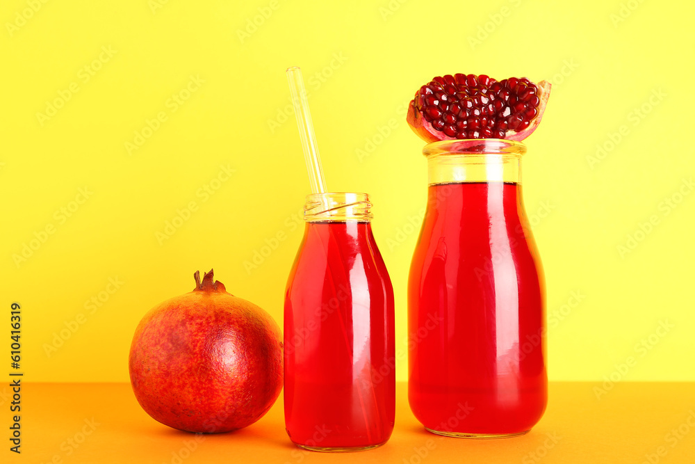 Bottles of fresh pomegranate juice on yellow background