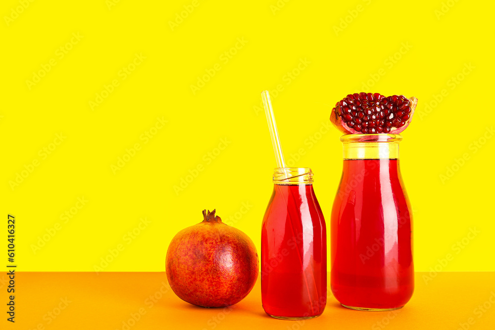 Bottles of fresh pomegranate juice on yellow background