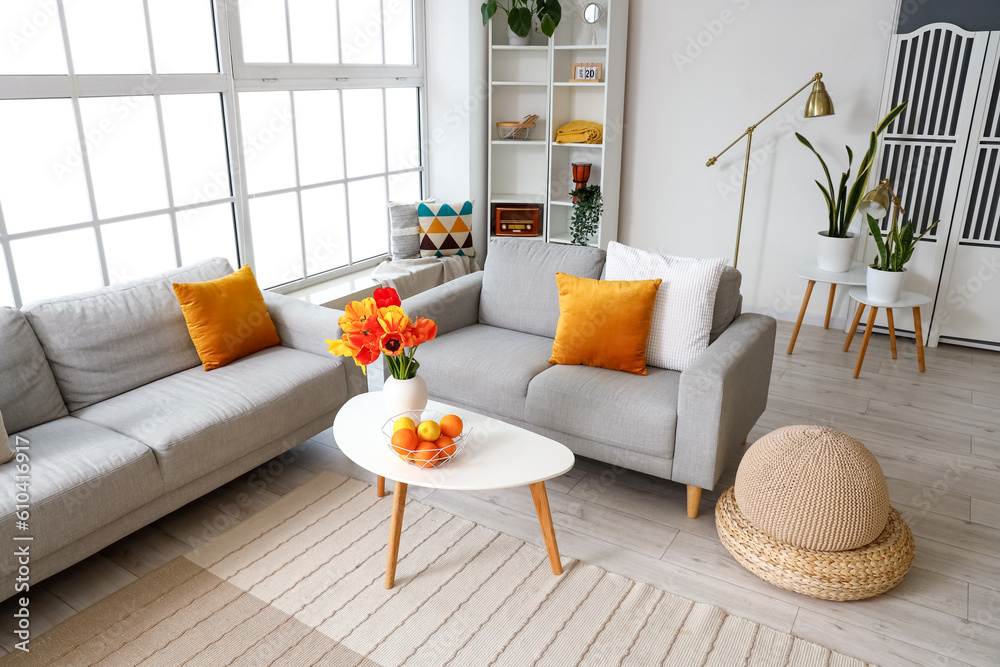 Interior of stylish living room with cozy sofas and tulip flowers on coffee table