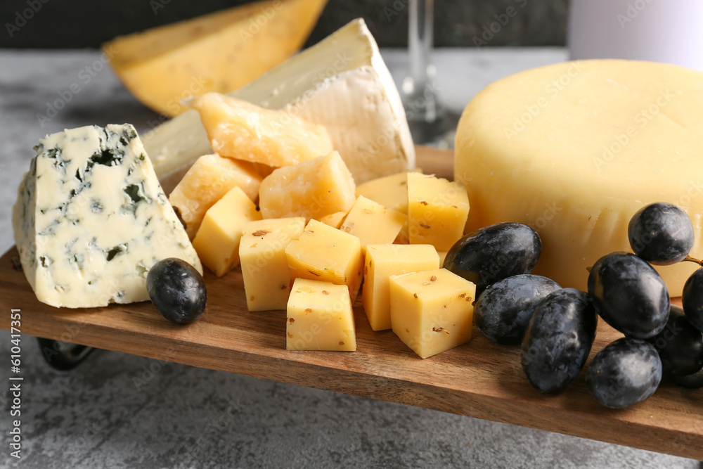 Wooden board with pieces of tasty cheese on table, closeup