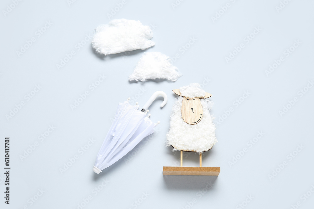 Creative composition with wooden toy sheep, clouds and mini umbrellas on white background