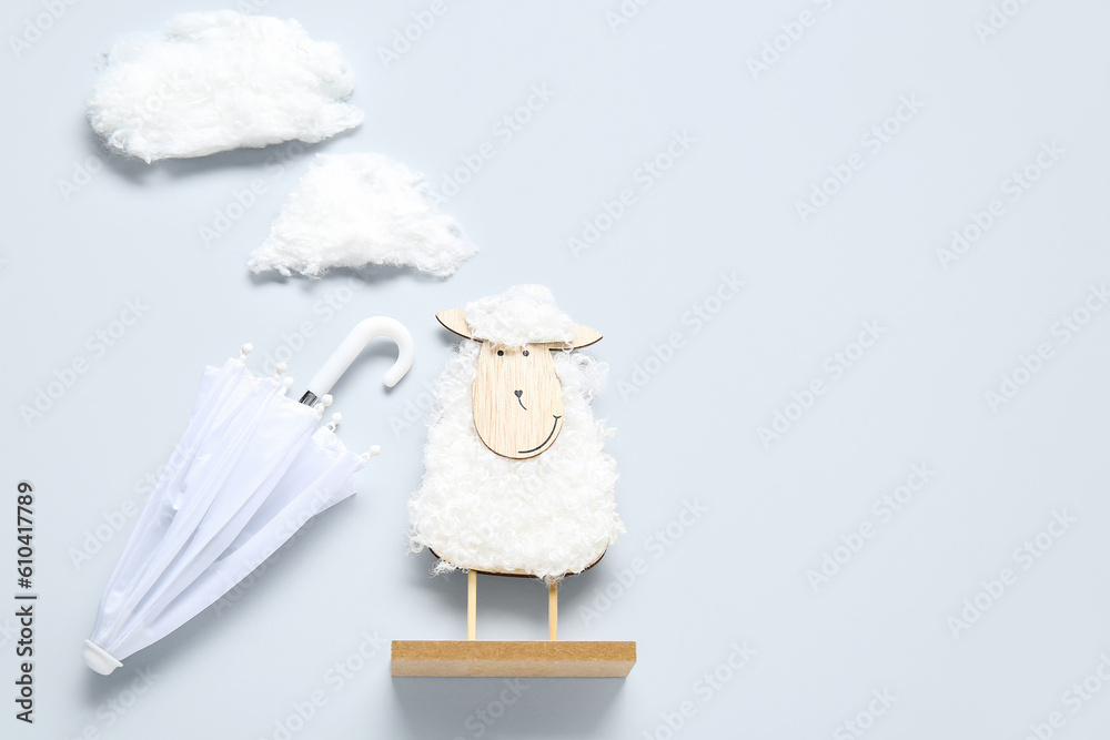 Creative composition with wooden toy sheep, clouds and mini umbrellas on white background