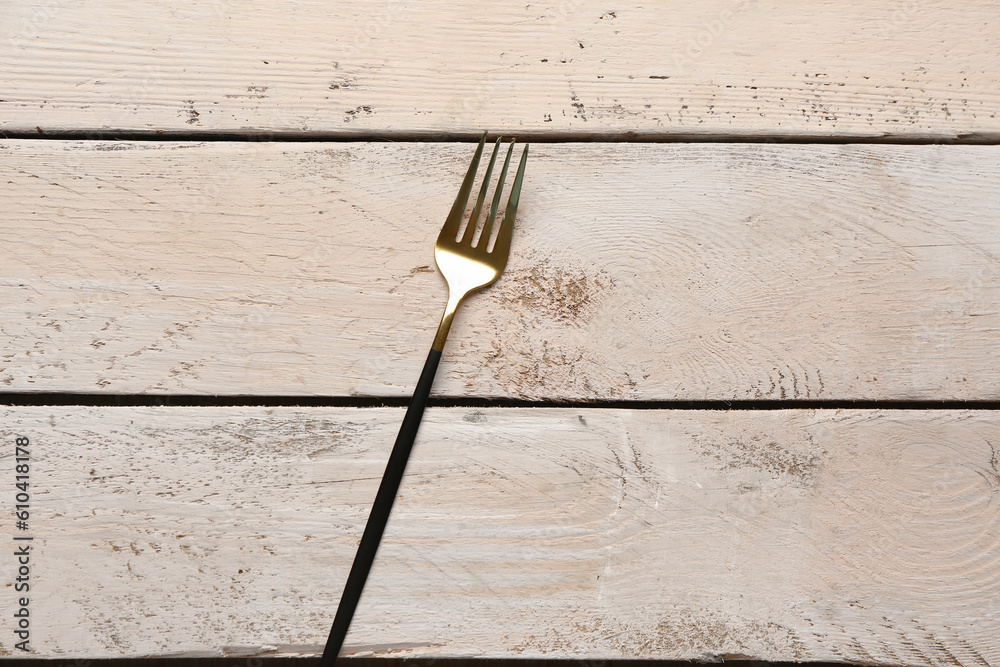 Golden fork with black handle on white wooden background