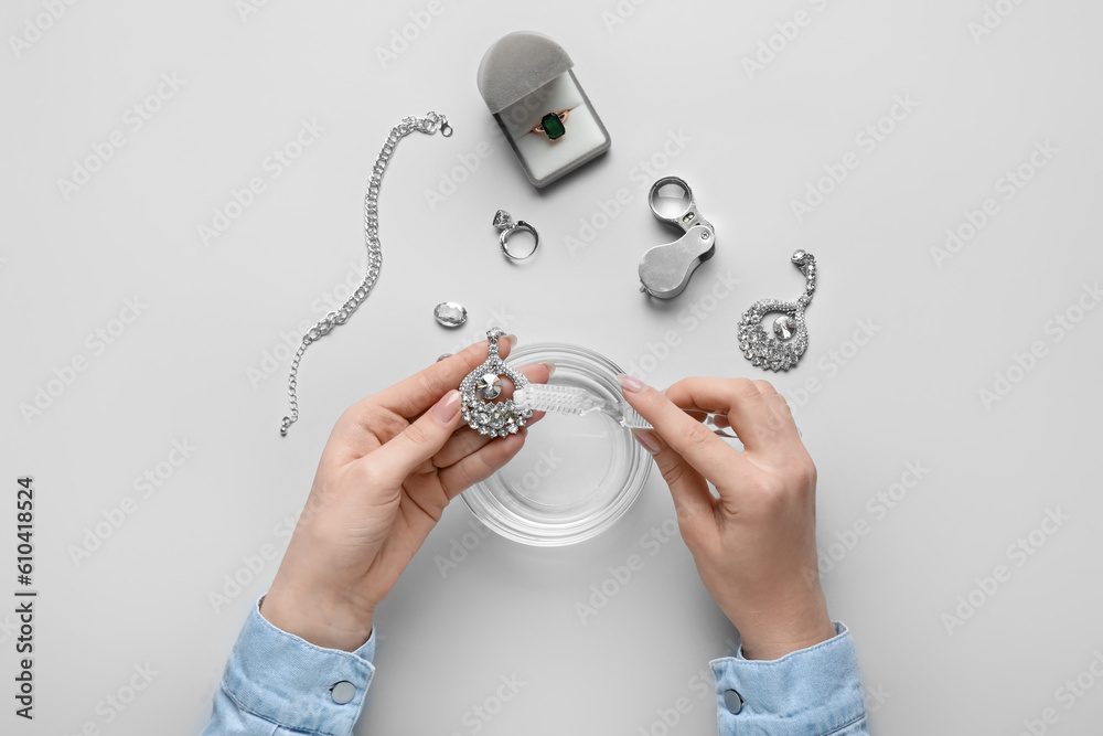 Woman cleaning beautiful jewelry with toothbrush on white background