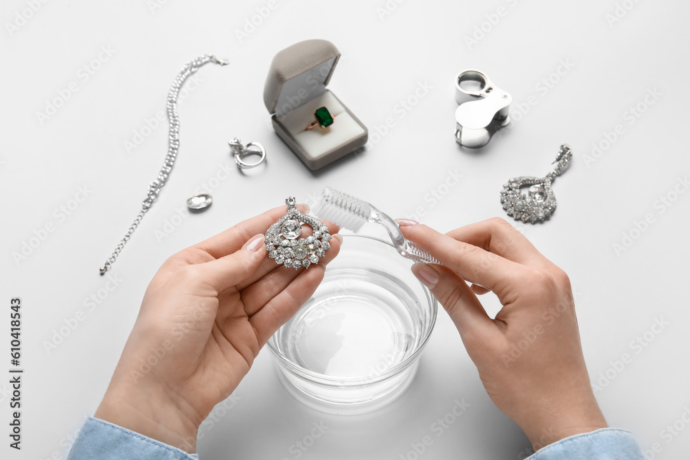 Woman cleaning beautiful jewelry with toothbrush on white background, closeup