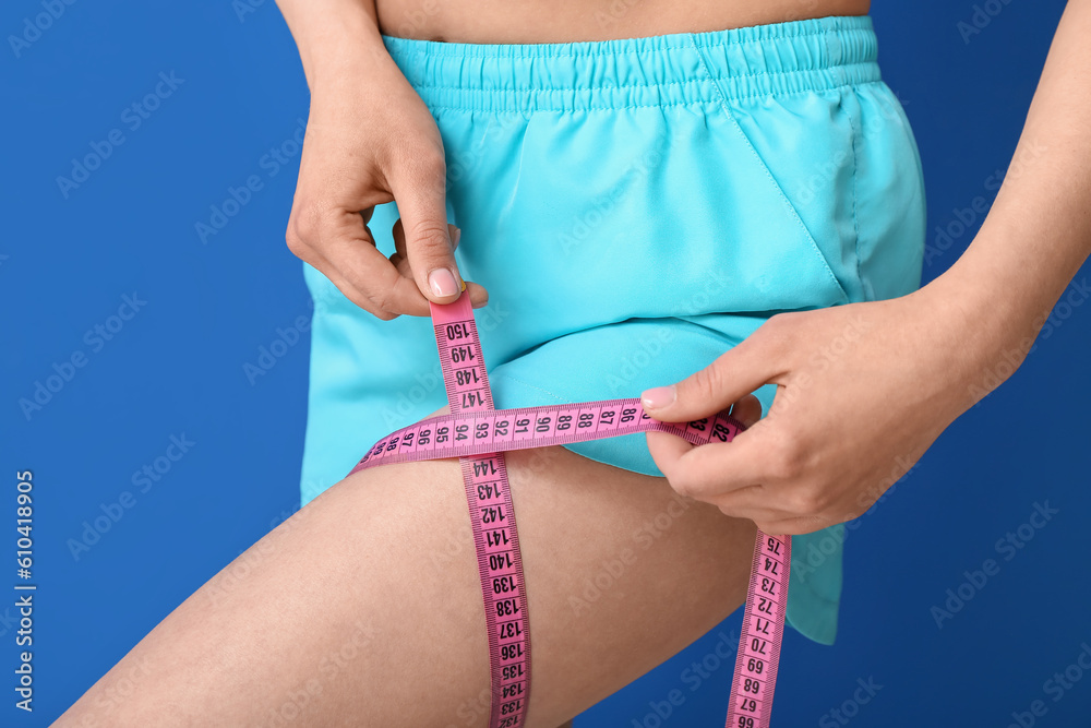 Young woman with measuring tape on blue background, closeup. Diet concept