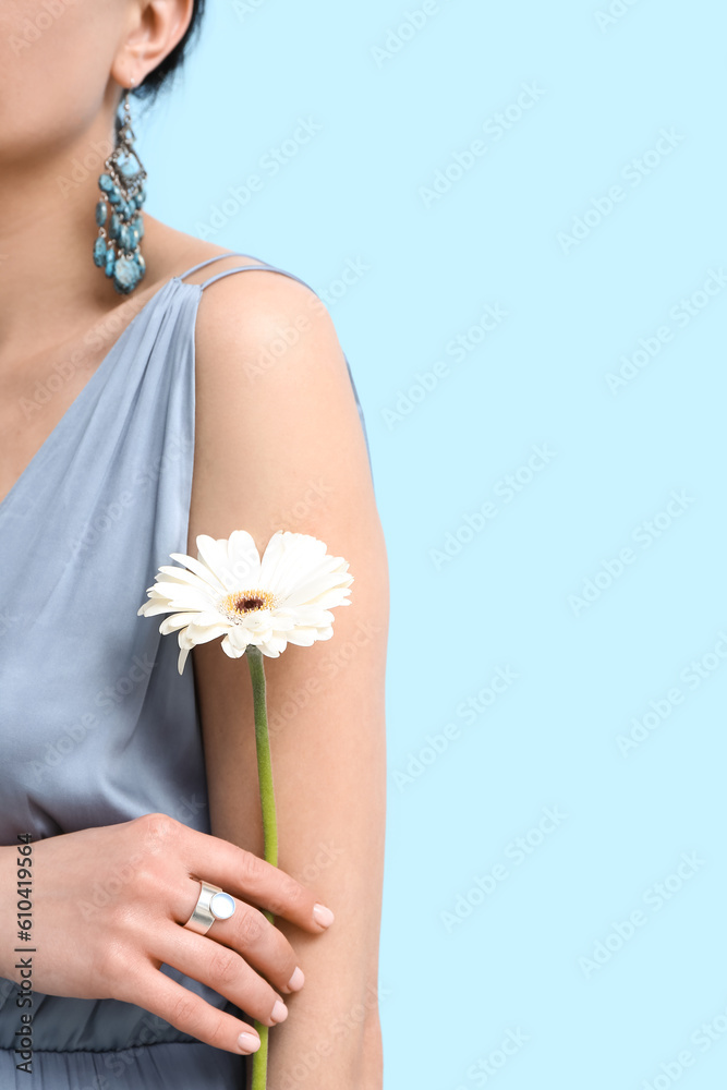 Beautiful woman with stylish jewelry and flower near blue wall