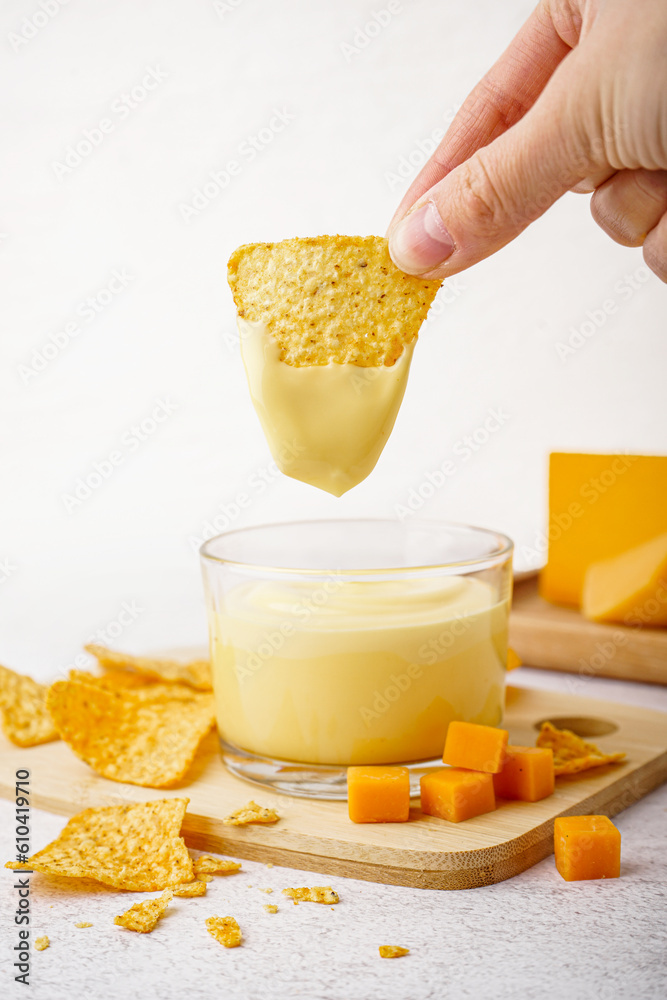 Female hand dipping nacho into tasty cheddar cheese sauce on table