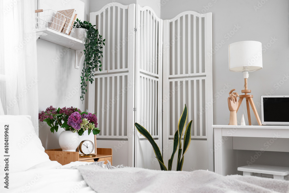 Interior of light bedroom with workplace and folding screen