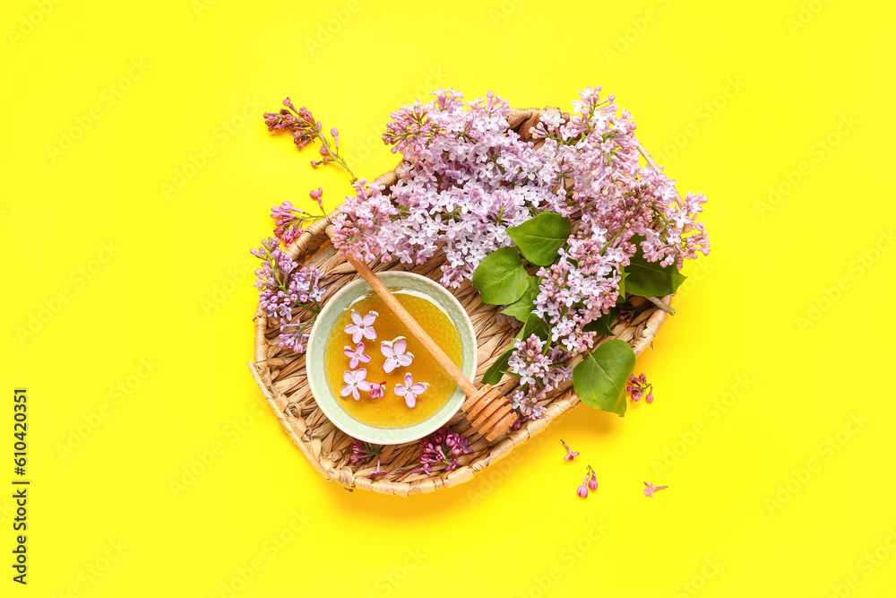 Basket with lilacs and bowl of honey on yellow background