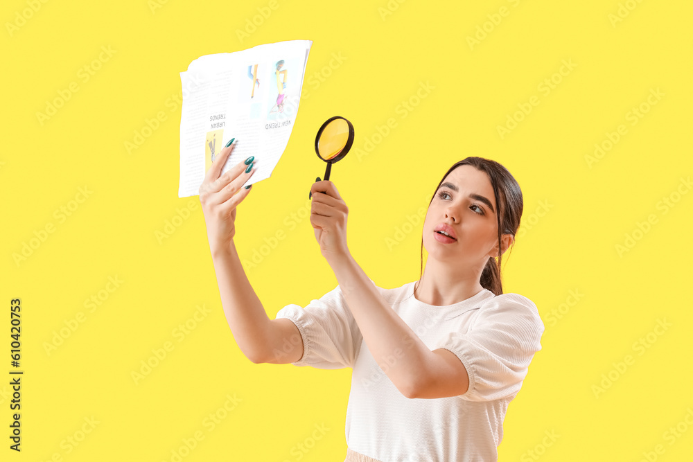 Young woman with magnifier reading newspaper on yellow background