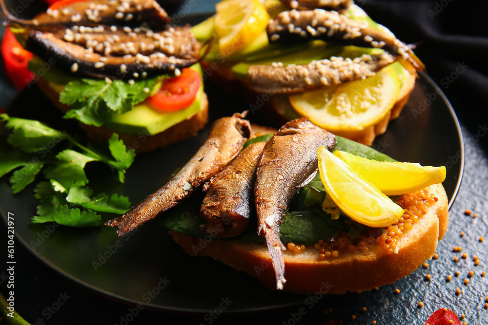 Plate of tasty sandwiches with canned smoked sprats on black background