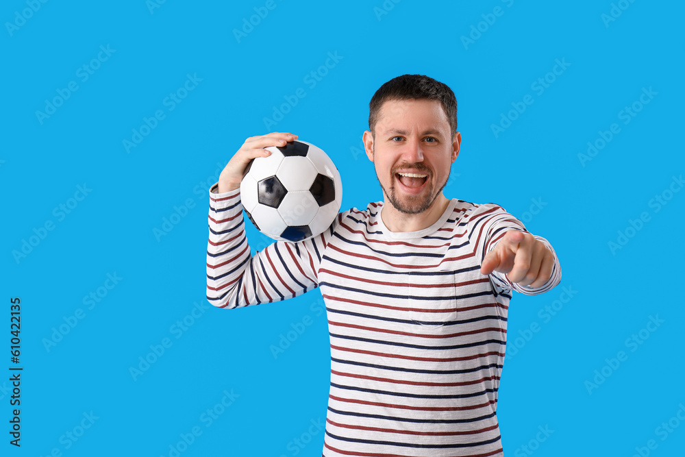 Man with soccer ball pointing at viewer on blue background