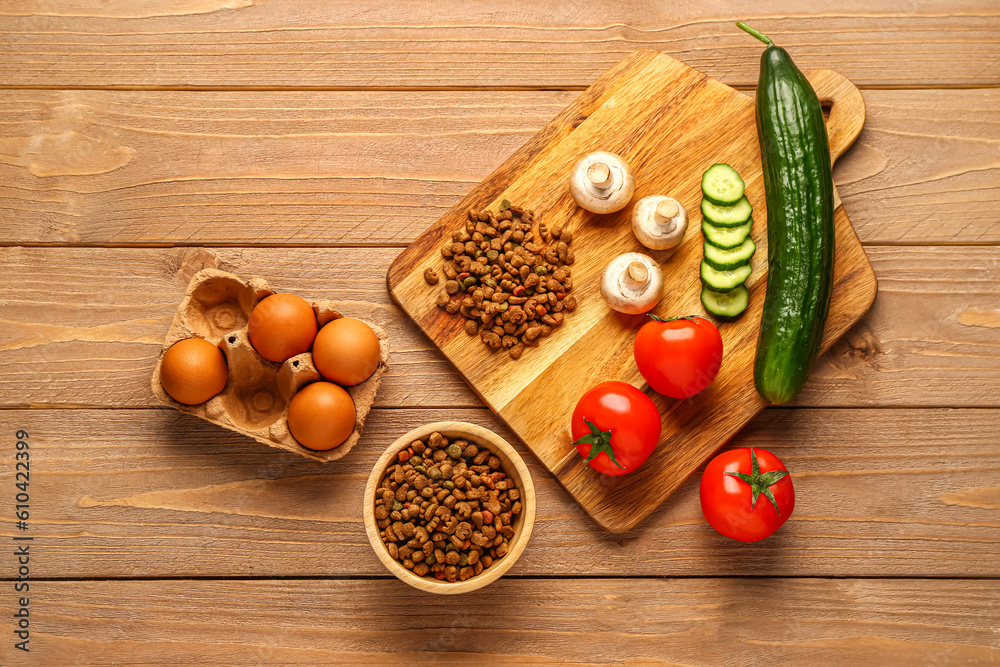 Bowl with dry pet food and natural products on wooden background