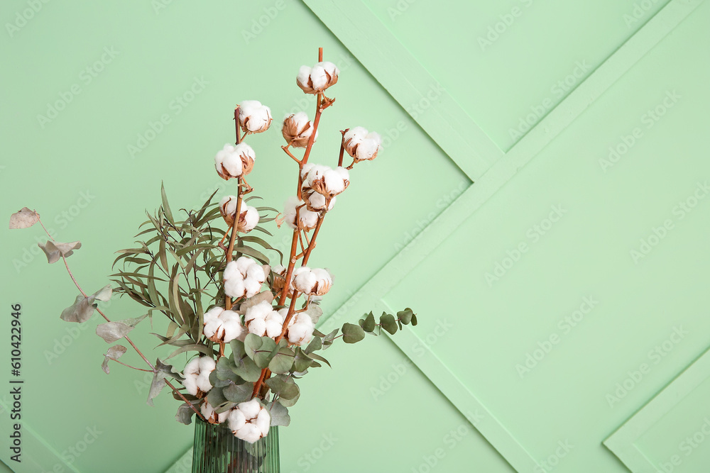 Vase of cotton sprig and eucalyptus near green wall