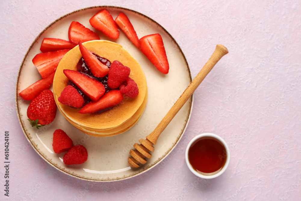 Plate with sweet pancakes, berries and honey on pink background