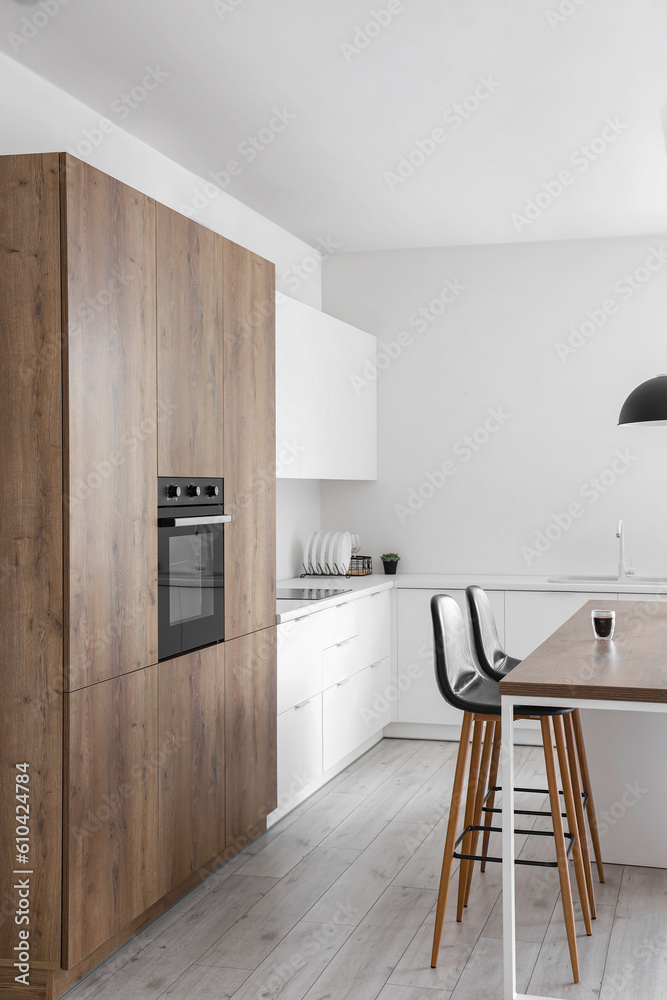 Interior of modern kitchen with island, built-in oven and white counters