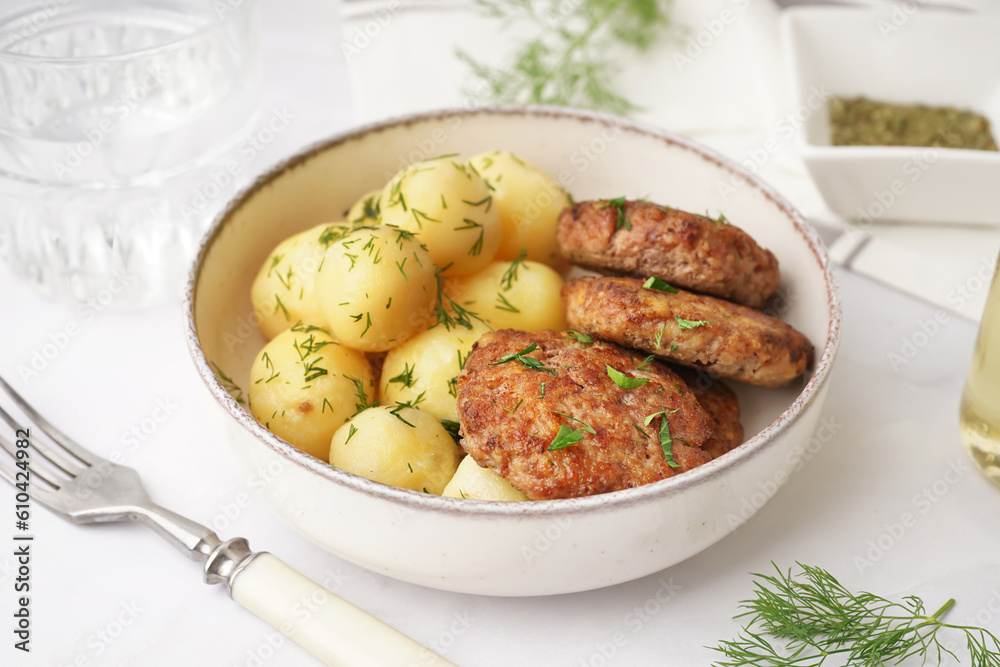 Bowl with cutlets, boiled baby potatoes and dill on white table in kitchen