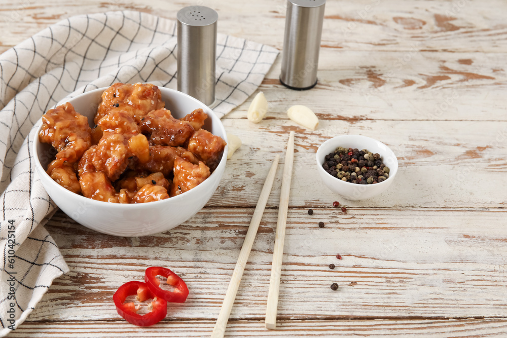 Tasty sweet and sour chicken in bowl with spices on light wooden background