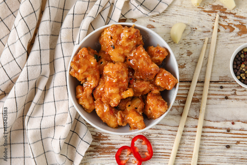 Bowl with tasty sweet and sour chicken on light wooden background, closeup