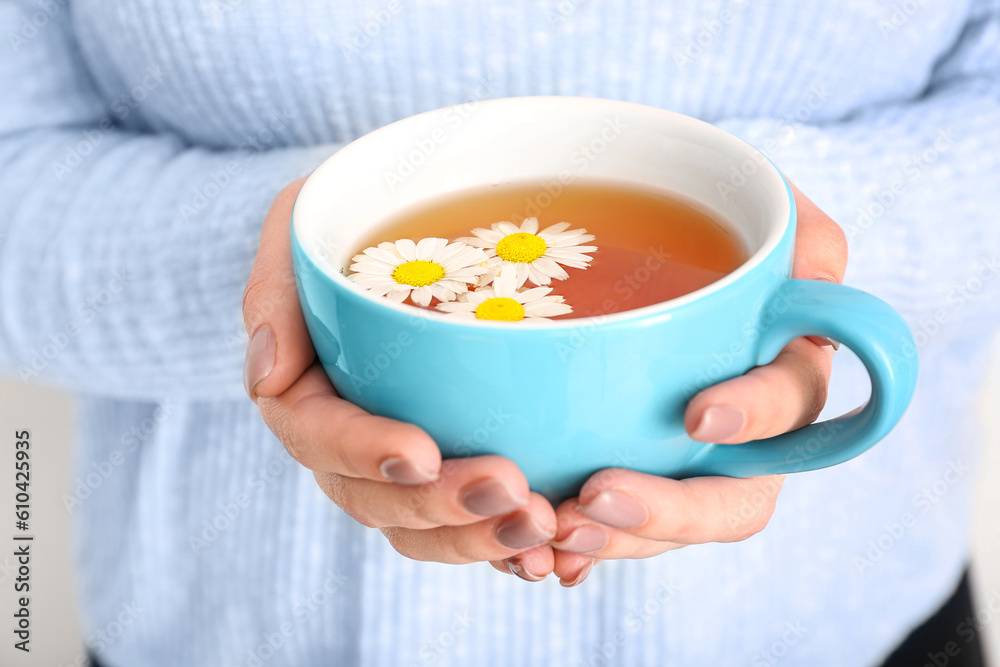 Beautiful young woman with cup of chamomile tea near white wall