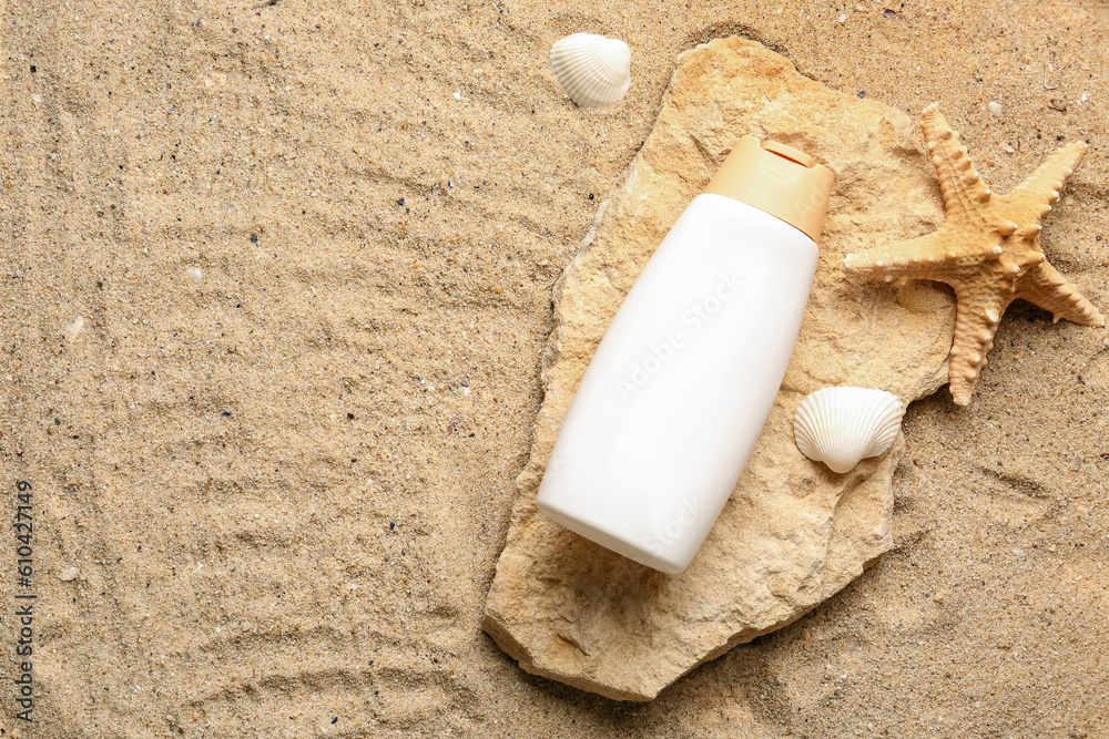 Bottle of sunscreen cream at stone with seashells and starfish on sand