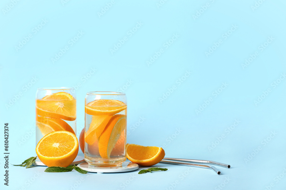 Glasses of infused water with orange slices on blue background