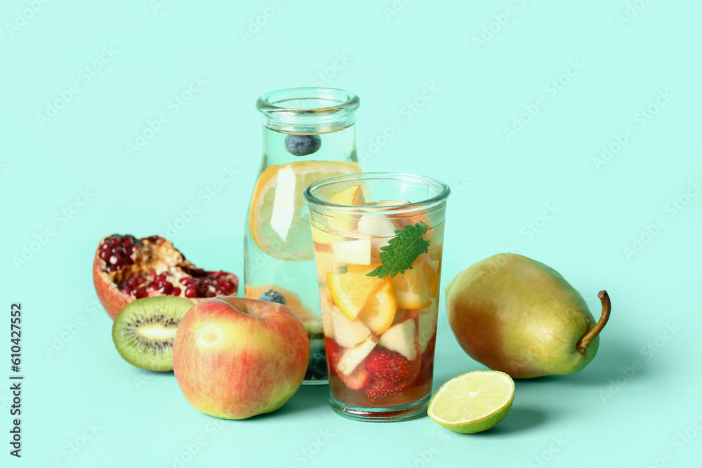 Glass and bottle of infused water with different sliced fruits on blue background