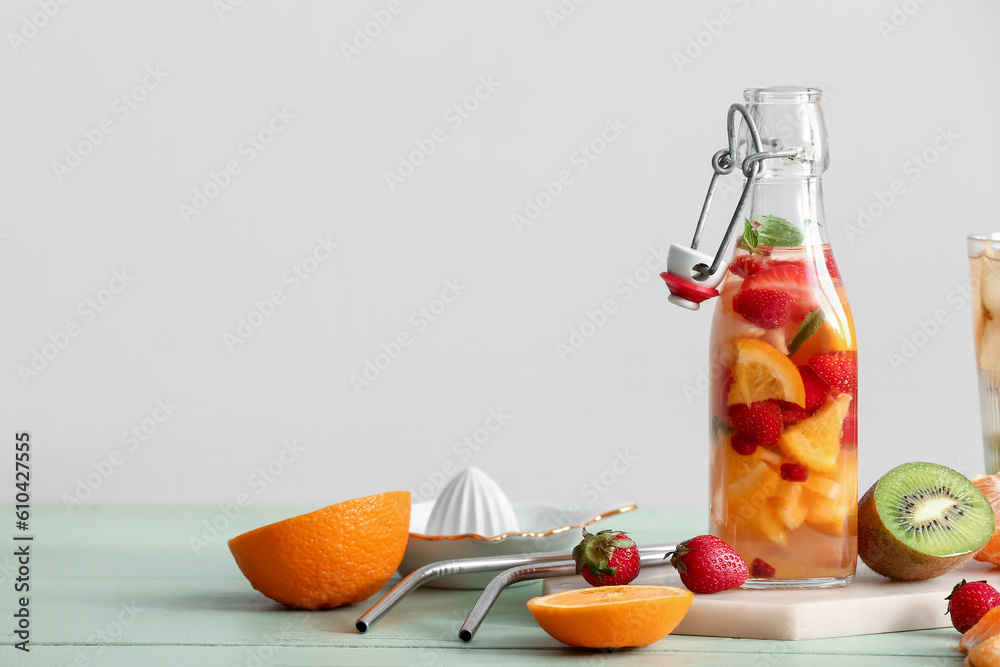 Bottle of infused water with different sliced fruits on green wooden table