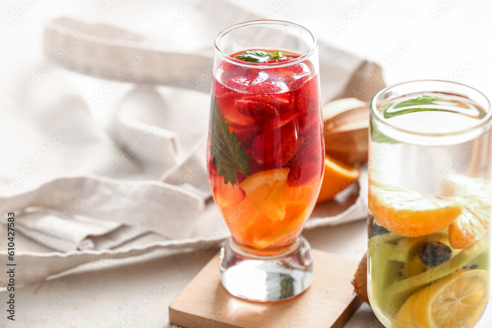 Glasses of infused water with different sliced fruits on white table