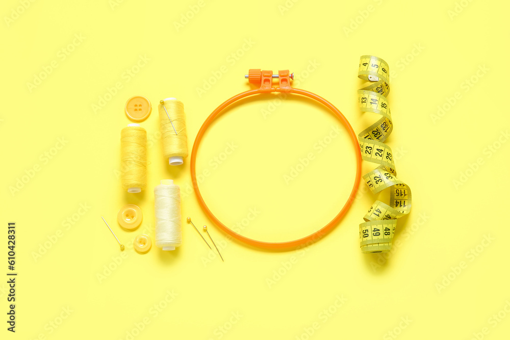 Embroidery hoop with thread spools and measuring tape on yellow background