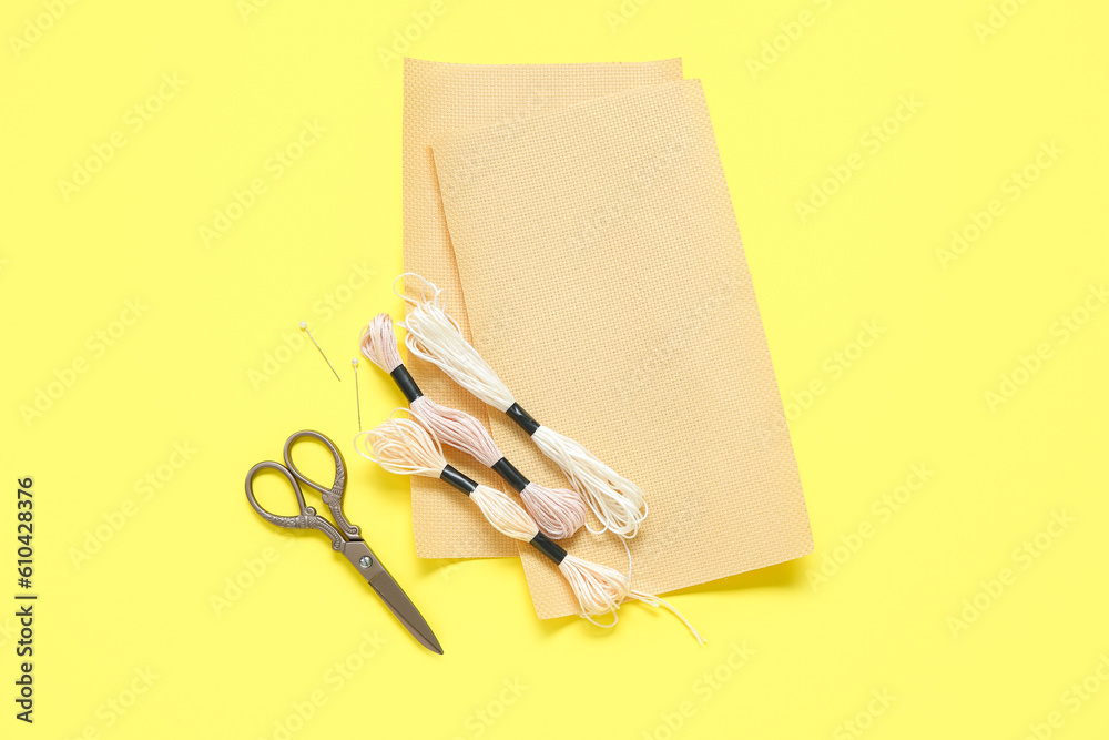 Canvas with scissors, mouline threads and pins on yellow background