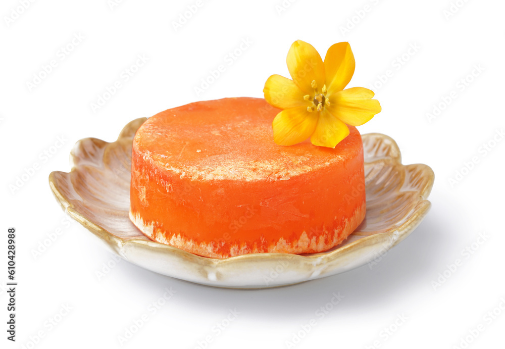 Plate with orange solid shampoo bar and flower on white background