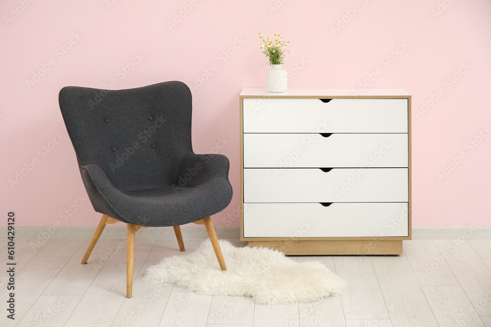 Dark grey armchair with dresser, fluffy rug and daisy near pink wall