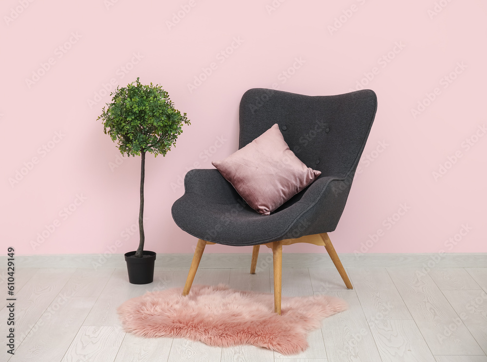 Dark grey armchair with pillow, fluffy rug and houseplant near pink wall