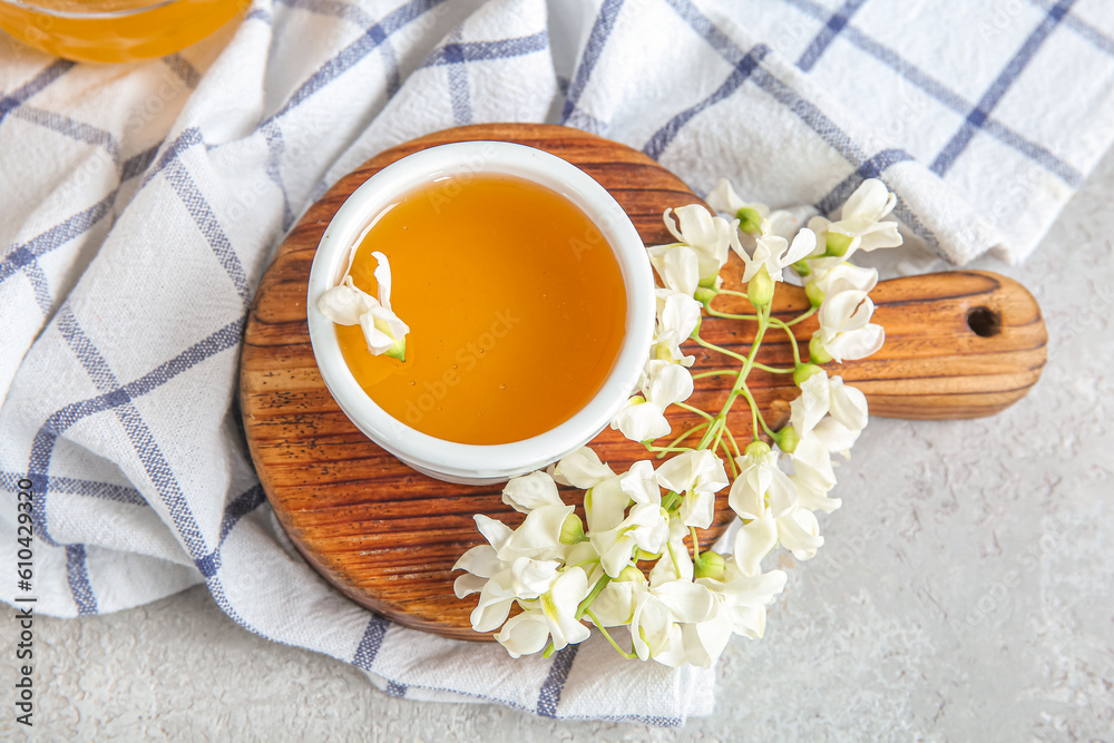 Bowl of honey with flowers of acacia on light background, closeup