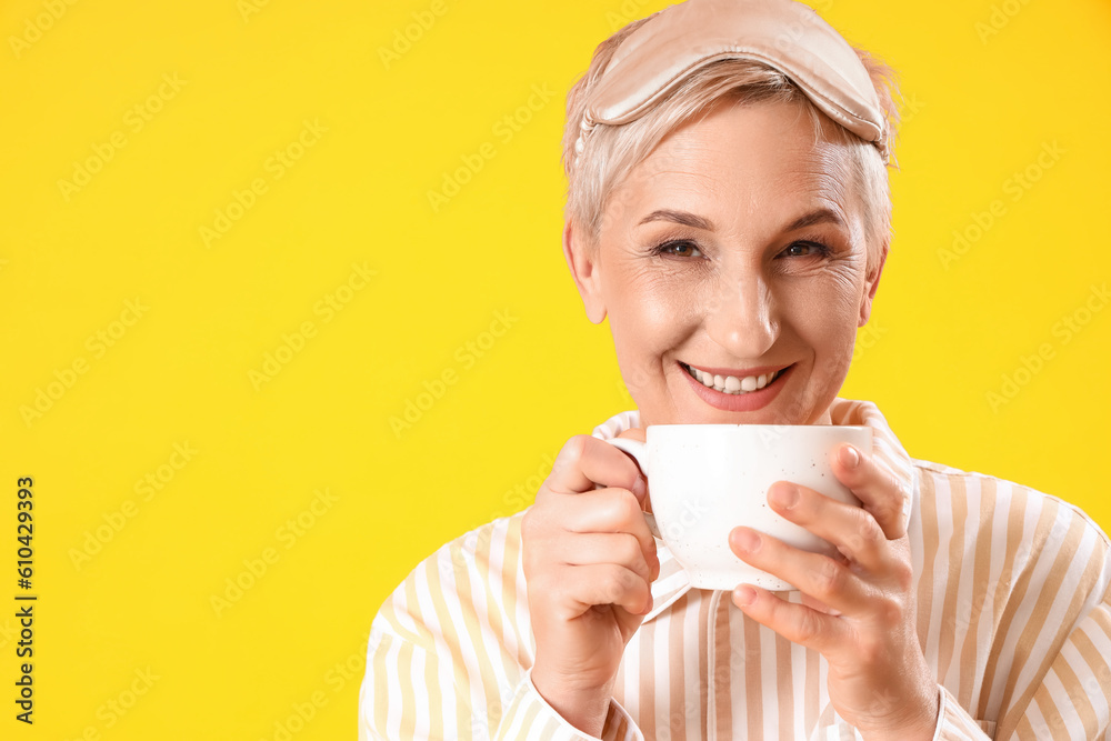 Mature woman in pajamas with cup of coffee on yellow background, closeup