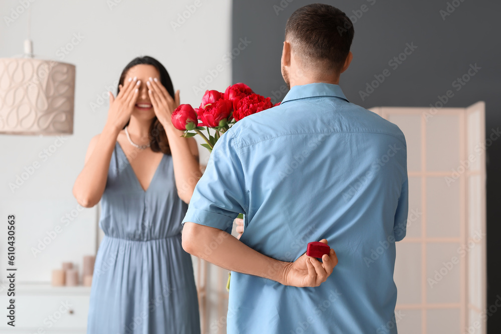 Young man with flowers proposing to his girlfriend at home, back view