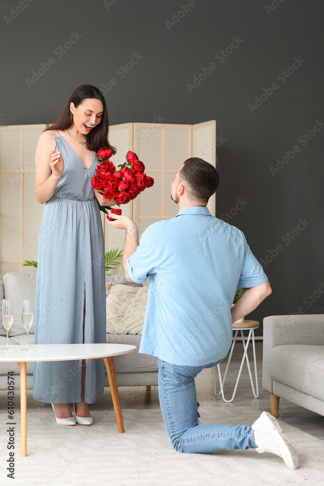 Young man proposing to his girlfriend with flowers at home