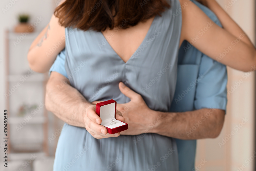 Young man with engagement ring hugging his girlfriend at home, closeup