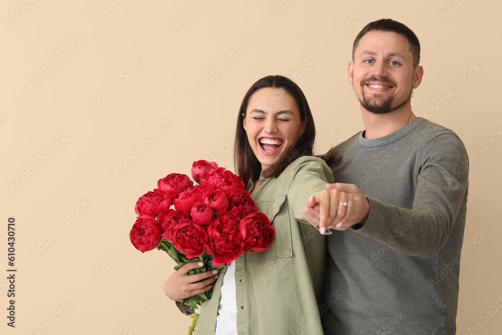 Happy engaged couple with flowers on beige background