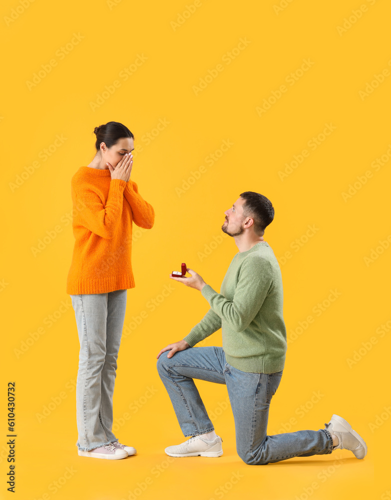 Young man proposing to his girlfriend on yellow background